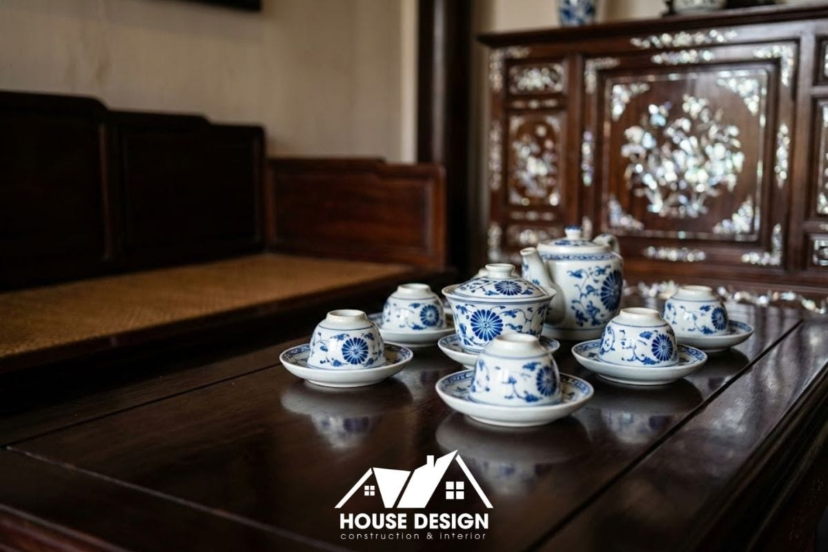 Cận cảnh bộ ấm trà cổ trên bàn gỗ, phía sau là sập gụ và tủ chè khảm ốc tinh xảo.