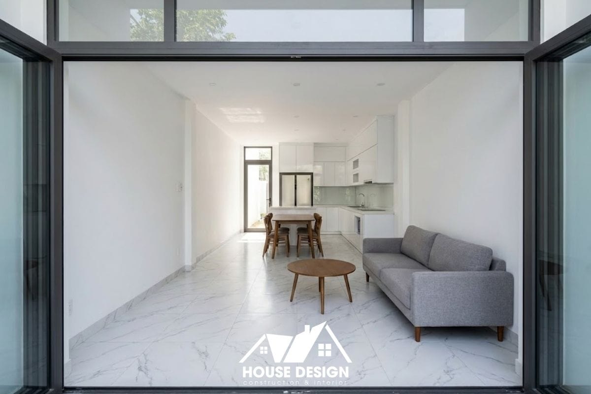 Toàn cảnh tầng 1 nhà ống 2 tầng sau cải tạo với phòng khách nối liền phòng bếp, sàn gạch vân đá chạy suốt tạo chiều sâu.